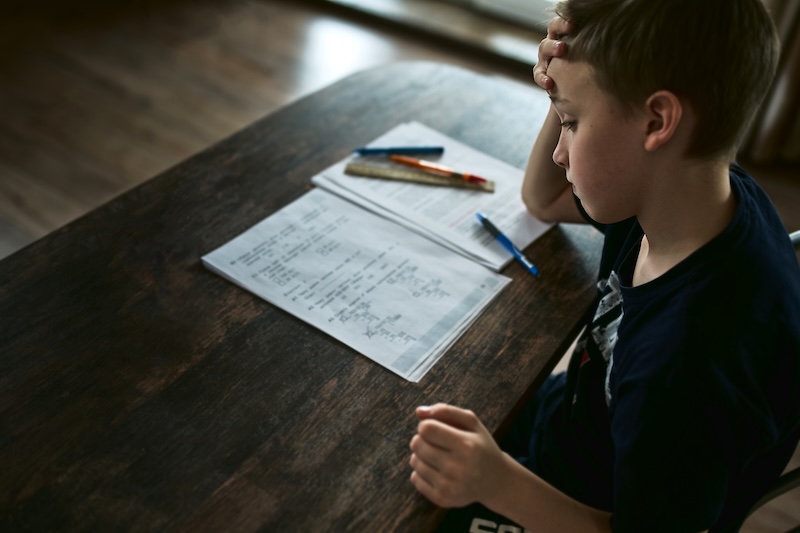Schüler sitzt mit Matheaufgaben am Tisch, ein Bild für Hausaufgabenstress bei Dyskalkulie und schulische Entlastung durch HEBO